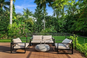 An outdoor seating area with a sofa and chairs, surrounded by lush greenery and tall trees. - Serene Escape on McGregor | Fort Myers (Fort Myers)