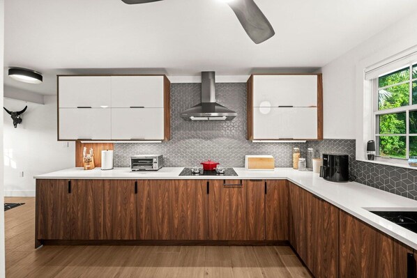 A modern kitchen with wooden cabinets, a central island, and a view of greenery outside. - Serene Escape on McGregor | Fort Myers (Fort Myers)