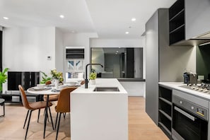A modern kitchen with a central island, a dining area with a table and chairs, and a built-in oven. - Level 34 City View 2 Bedroom (Melbourne)