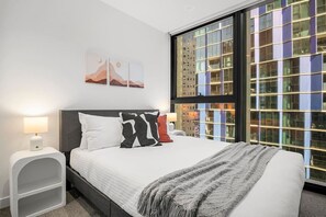 A modern hotel room with a large bed, two bedside tables, a nightstand, and a large window with a city view. - Level 34 City View 2 Bedroom (Melbourne)