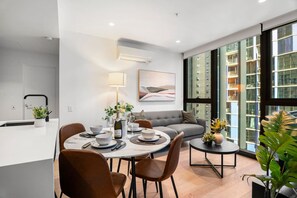 A modern hotel room with a dining area, a sofa, and large windows offering a city view. - Level 34 City View 2 Bedroom (Melbourne)