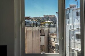 A view through a window of a building with balconies, a clear sky, and a distant hill with ruins. - Psyrri Home, Acropolis View and Lycabettus Terrace (Athens)