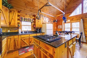Cocina de cabaña de madera con una isla central, armarios de madera y ollas colgantes.