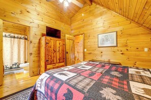 Un dormitorio de cabaña de troncos con una cama, un armario de madera, un cuadro enmarcado en la pared y una ventana con cortina.