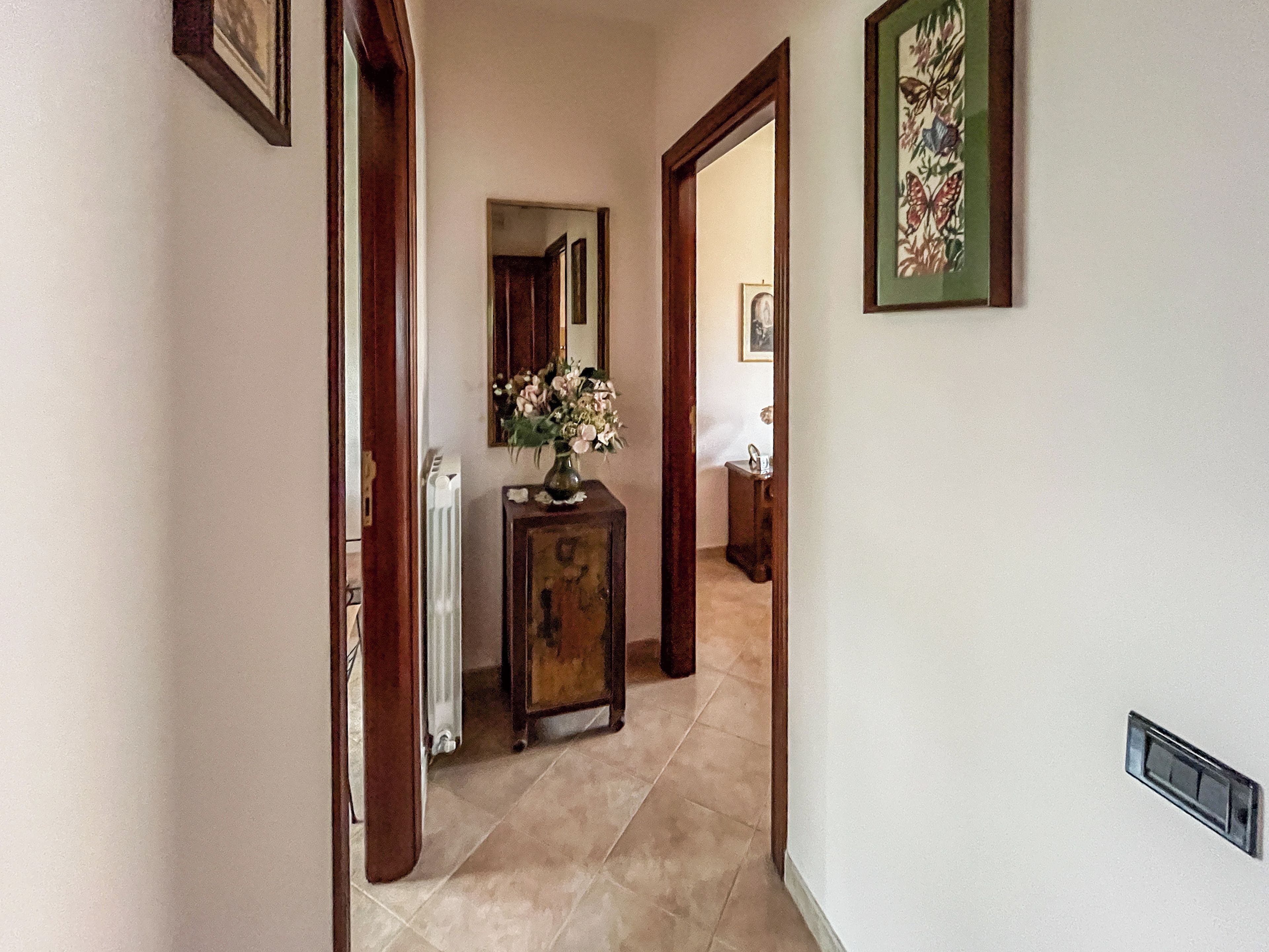 A hallway with a radiator, a wooden cabinet with a vase, and a framed picture on the wall.