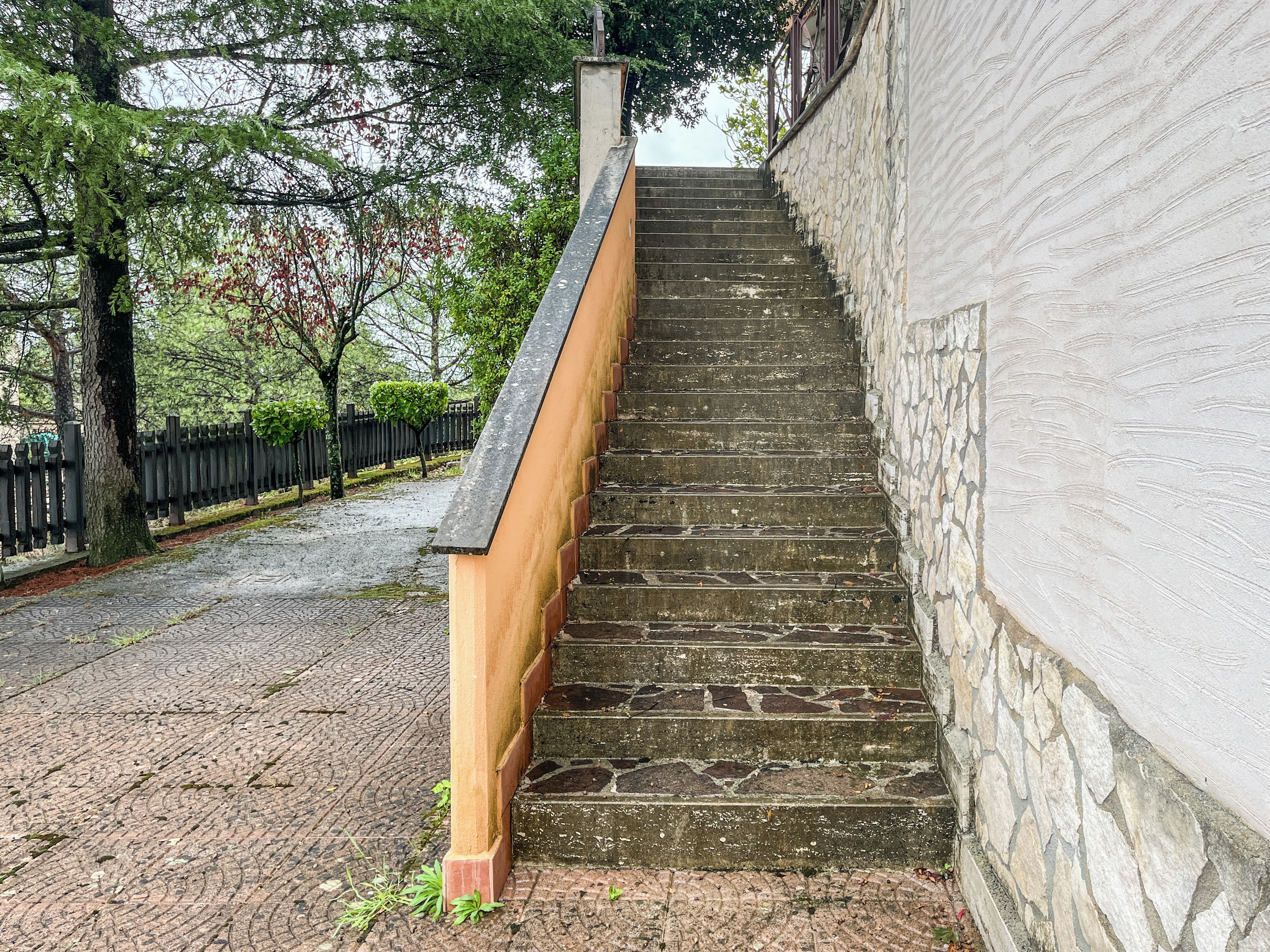 A staircase with stone steps and a wooden handrail, leading up to a white wall.