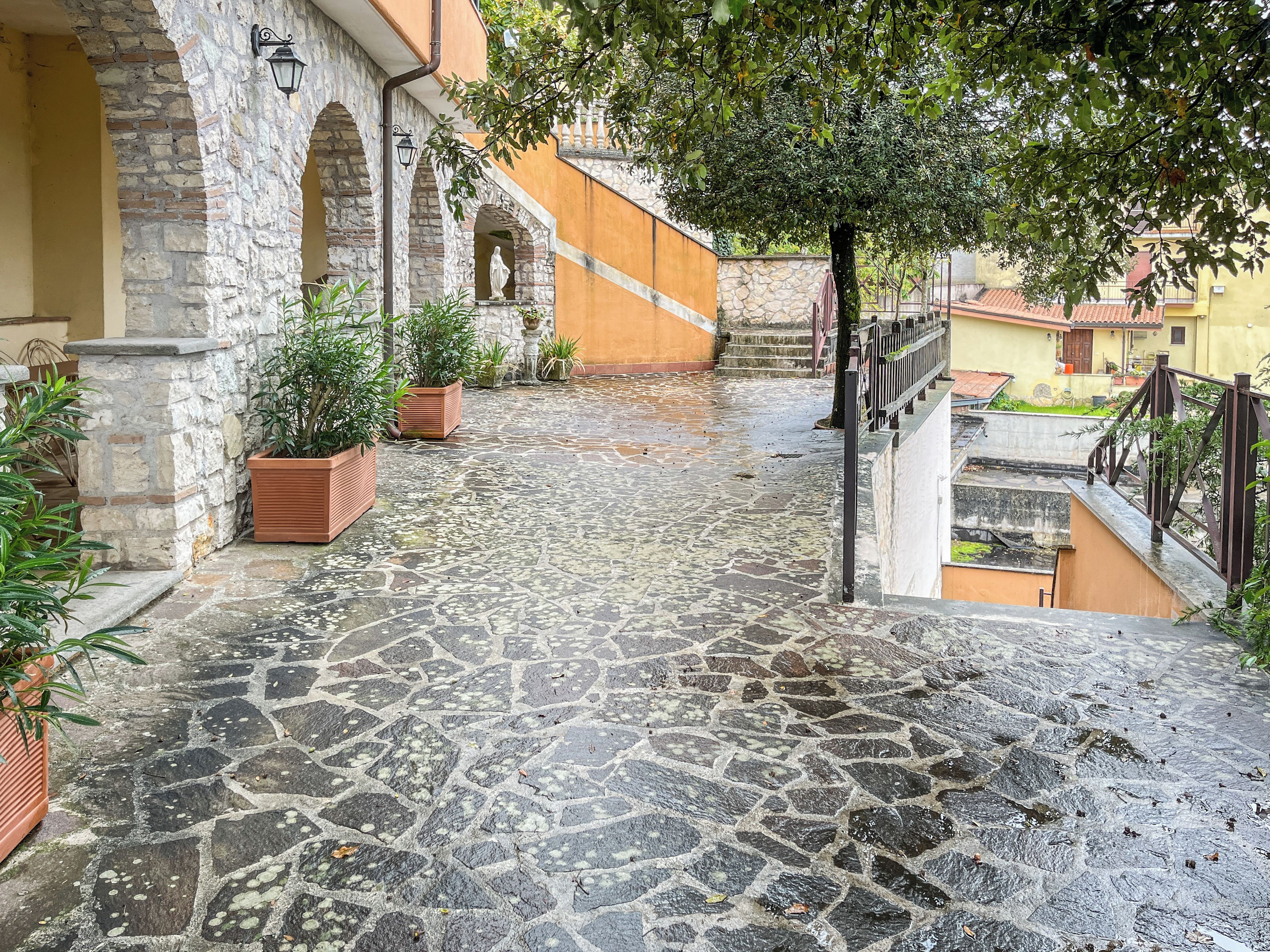A cobblestone courtyard with stone walls, potted plants, and a staircase leading to an upper level.