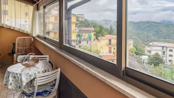 En balkon med bord og stole, der ud til et boligområde med bygninger og bakker.