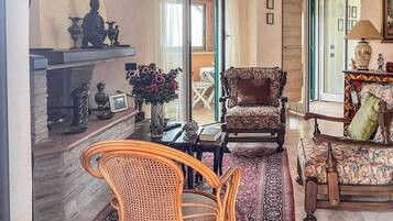 A living room with a fireplace, a patterned armchair, a rattan chair, and a coffee table.