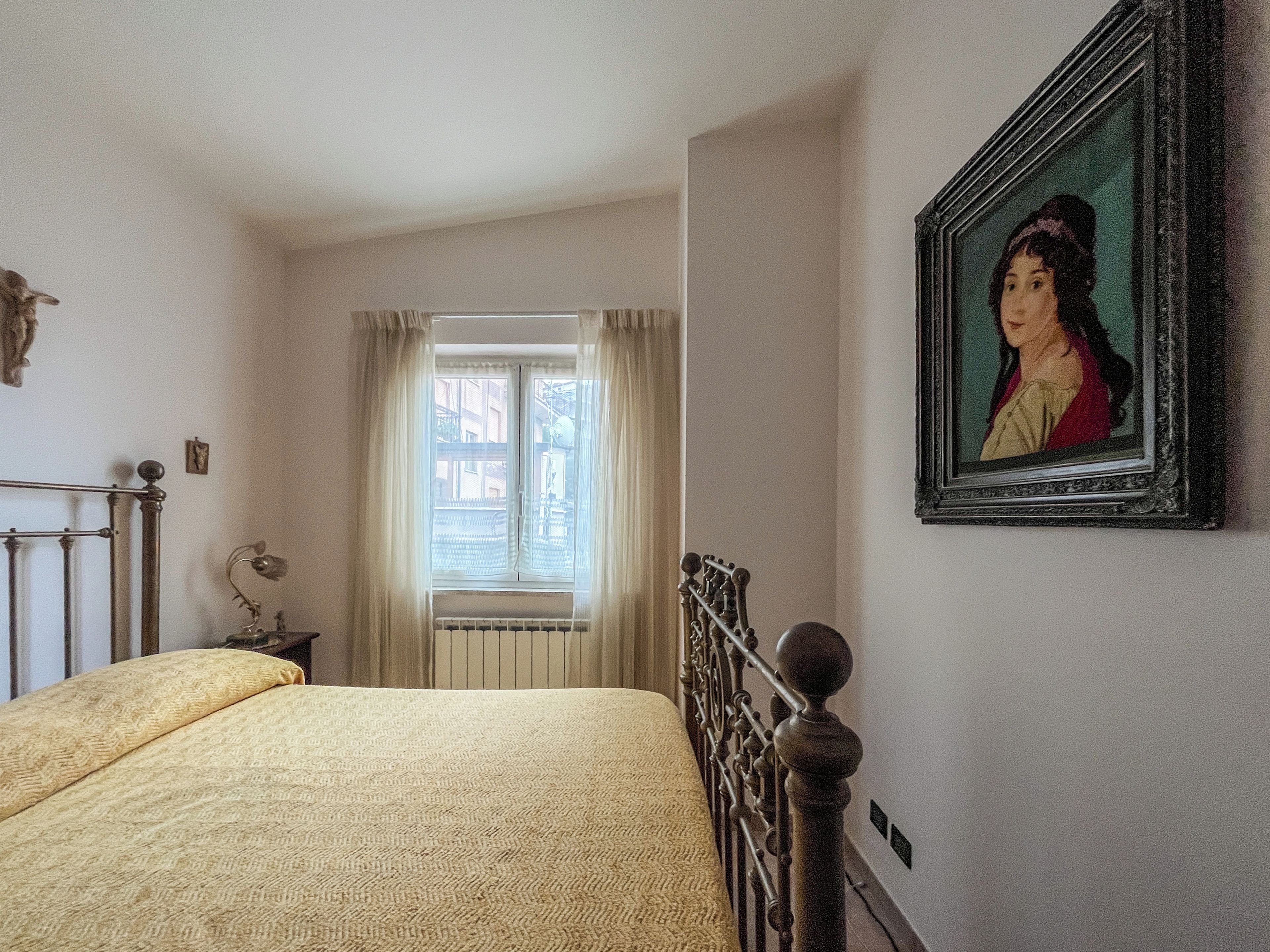 Une chambre à coucher avec un lit, une fenêtre avec des rideaux, un radiateur et un portrait encadré accroché au mur.