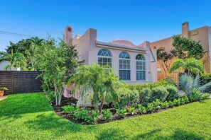A house with a garden, a wooden fence, and a clear blue sky. - Palm Beach Chic Pink Bungalow: King Bed (West Palm Beach)