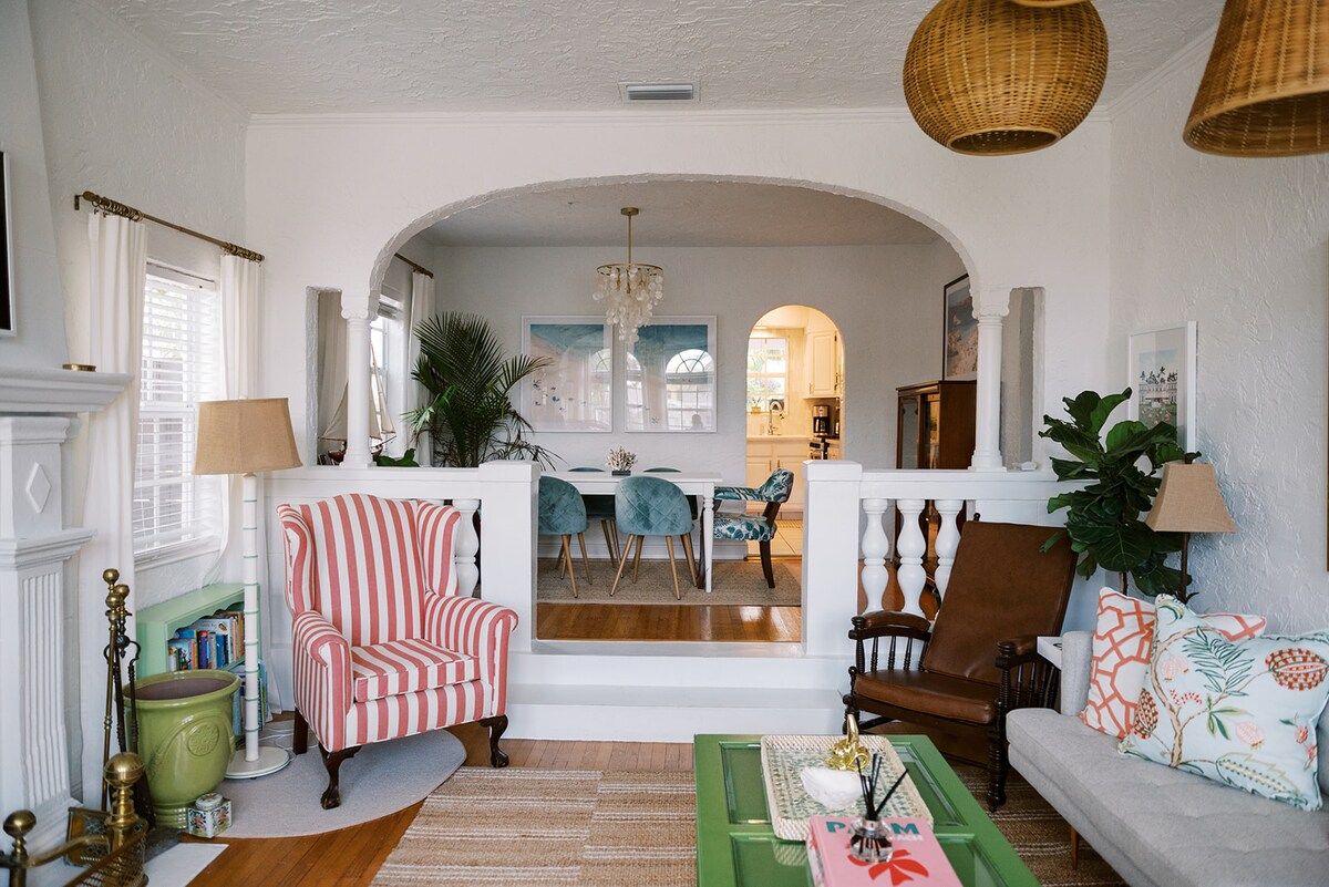 A living room with a fireplace, striped armchair, dining area, and a view into the kitchen.