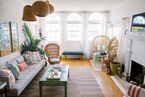 A cozy living room with a sofa, chairs, a fireplace, and large windows. - Palm Beach Chic Pink Bungalow: King Bed (West Palm Beach)
