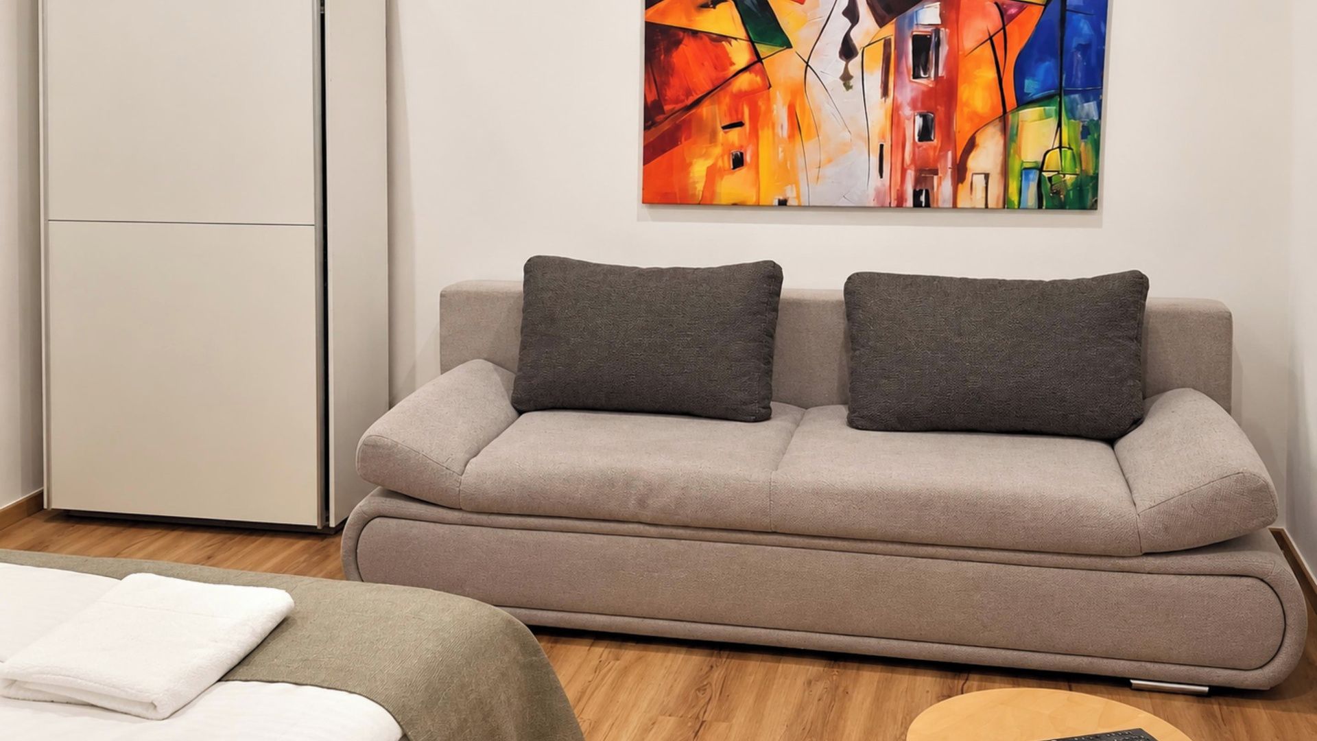 A modern living room with a sofa, two pillows, a white towel, and a colorful abstract painting on the wall.