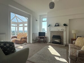 Een ruime woonkamer met een open haard, een televisie en een uitzicht door grote ramen.