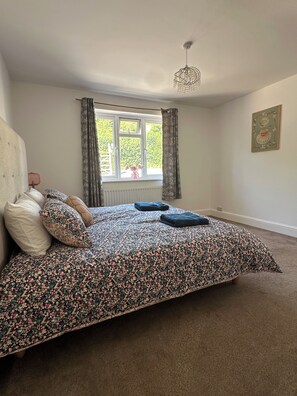 A bedroom with a bed, a window with curtains, a radiator, and a ceiling light fixture. - Honeycroft | Spacious Somerset Bungalow | Stunning Views | Dog Friendly (Rodney Stoke)