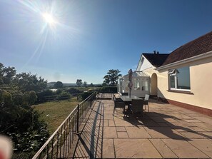 A patio with a table and chairs, a glass conservatory, and a view of the countryside. - Honeycroft | Spacious Somerset Bungalow | Stunning Views | Dog Friendly (Rodney Stoke)
