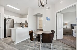 A modern kitchen with white cabinetry, a stainless steel refrigerator, and a central island with chairs. - Ascent 1 Bed Gym Pool Cabanas 2 Miles to Mayo Clinic (Phoenix)
