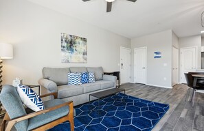 Ein Wohnzimmer mit grauem Sofa, blauen Kissen mit Muster, einem blauen Teppich und einem Holztisch.