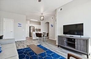 Una sala de estar moderna con televisor de pantalla plana, sofá gris y comedor con sillas y mesa.