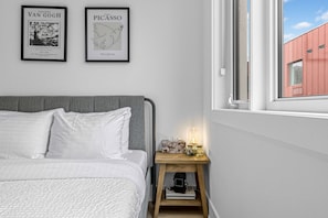 A bedroom with a bed, a nightstand with a lamp, and two framed artworks on the wall. - 
Furnished 2 Bedroom Townhouse in Kensington Market (Toronto)
