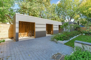 A modern building with two garage doors, a paved driveway, and bicycles parked outside. - 
Furnished 2 Bedroom Townhouse in Kensington Market (Toronto)