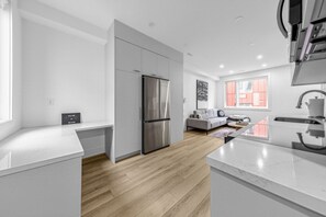 Une cuisine moderne dotée d’un réfrigérateur encastré, d’un plancher en bois et d’un canapé gris dans le salon attenant.