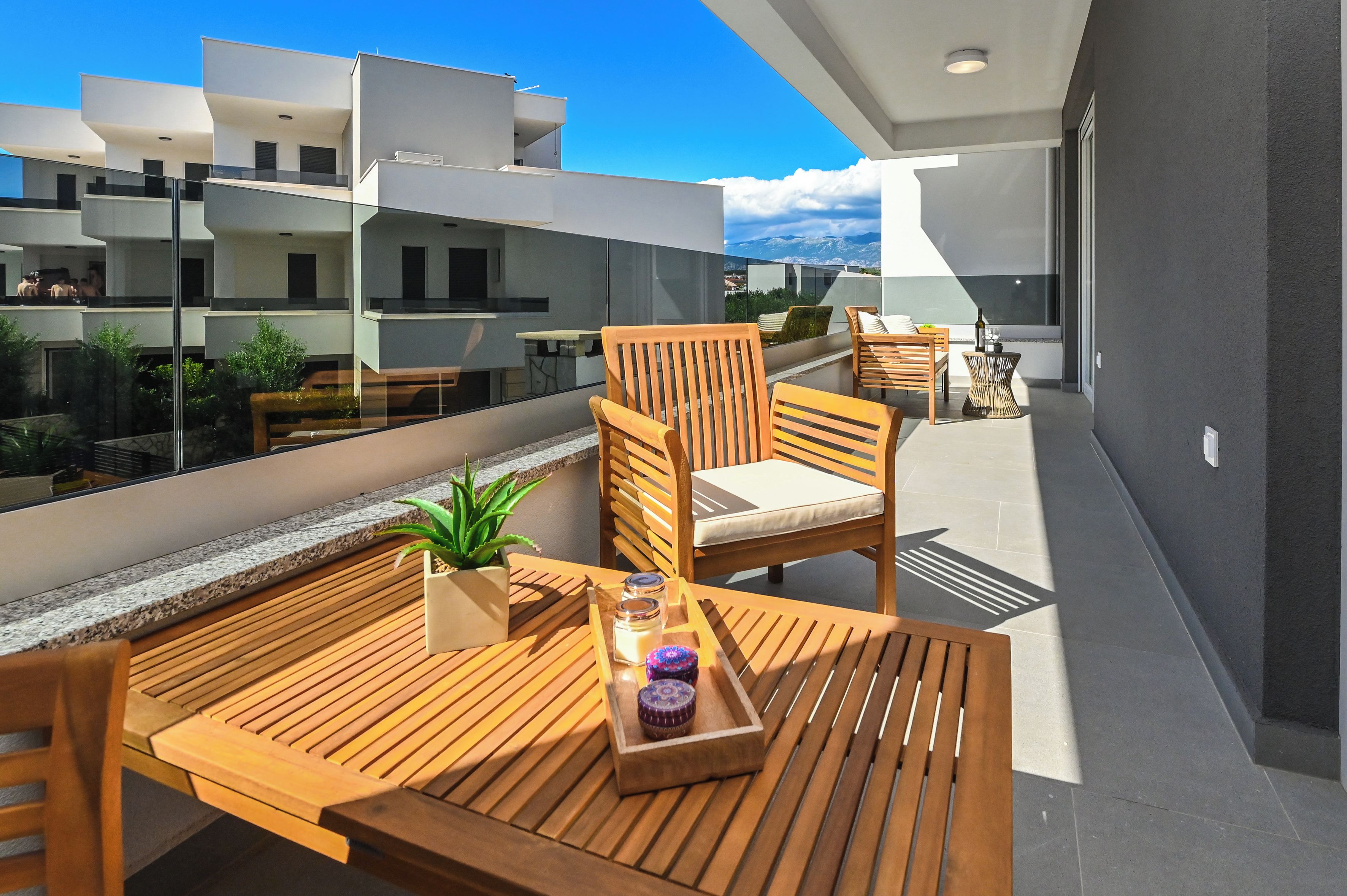 A modern outdoor balcony with wooden furniture, a small plant, and a tray with candles.