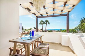A terrace with a table and chairs, overlooking a coastal view with palm trees and a clear sky. - Villa Gardenia Vista (Albufeira)