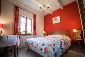 Quarto com cama, duas mesas de cabeceira, janela com cortinas, um candelabro e um quadro na parede.
