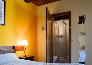Quarto de hotel com cama, mesa de cabeceira com abajur, banheiro com chuveiro e vaso sanitário.