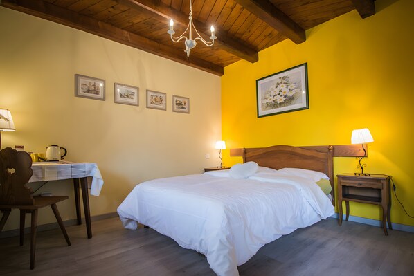 Quarto de hotel com cama, escrivaninha, cadeira, mesa de cabeceira e um candelabro.