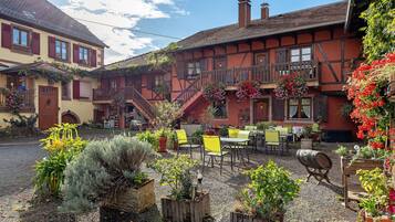 A courtyard with outdoor seating, a building with a balcony, and a clear sky.