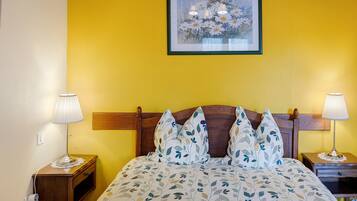 A hotel room with a bed, two bedside lamps, a wooden headboard, a wall-mounted picture, and a textured yellow wall.