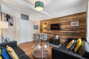 Uma sala de estar moderna com parede de madeira, sofá de couro preto, mesa de centro de vidro e porta branca.