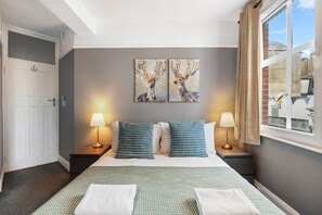 A hotel room with a bed, two nightstands, two lamps, and two wall-mounted paintings. - Hastings Buzz | By My Getaways (Hastings)