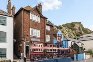A traditional pub with a sign reading 'The Dolphin Inn' and outdoor seating with umbrellas. - Hastings Buzz | By My Getaways (Hastings)