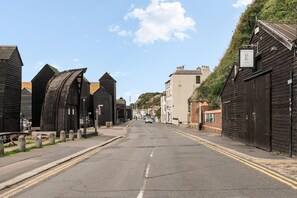 A street lined with traditional black wooden buildings, a clear sky, and a road with double yellow lines. - Hastings Buzz | By My Getaways (Hastings)