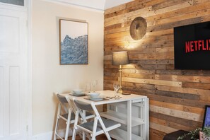 A dining area with a wooden wall, a framed artwork, a table set with plates and glasses, and a television displaying 'NETFLIX'. - Hastings Buzz | By My Getaways (Hastings)
