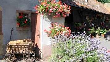 Un bâtiment rustique, avec une charrette remplie de foin, une brouette en bois et une variété de plantes en pot, dont de la lavande.