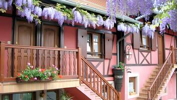 Un bâtiment doté d’un balcon, d’un escalier en bois et de fleurs violettes suspendues.
