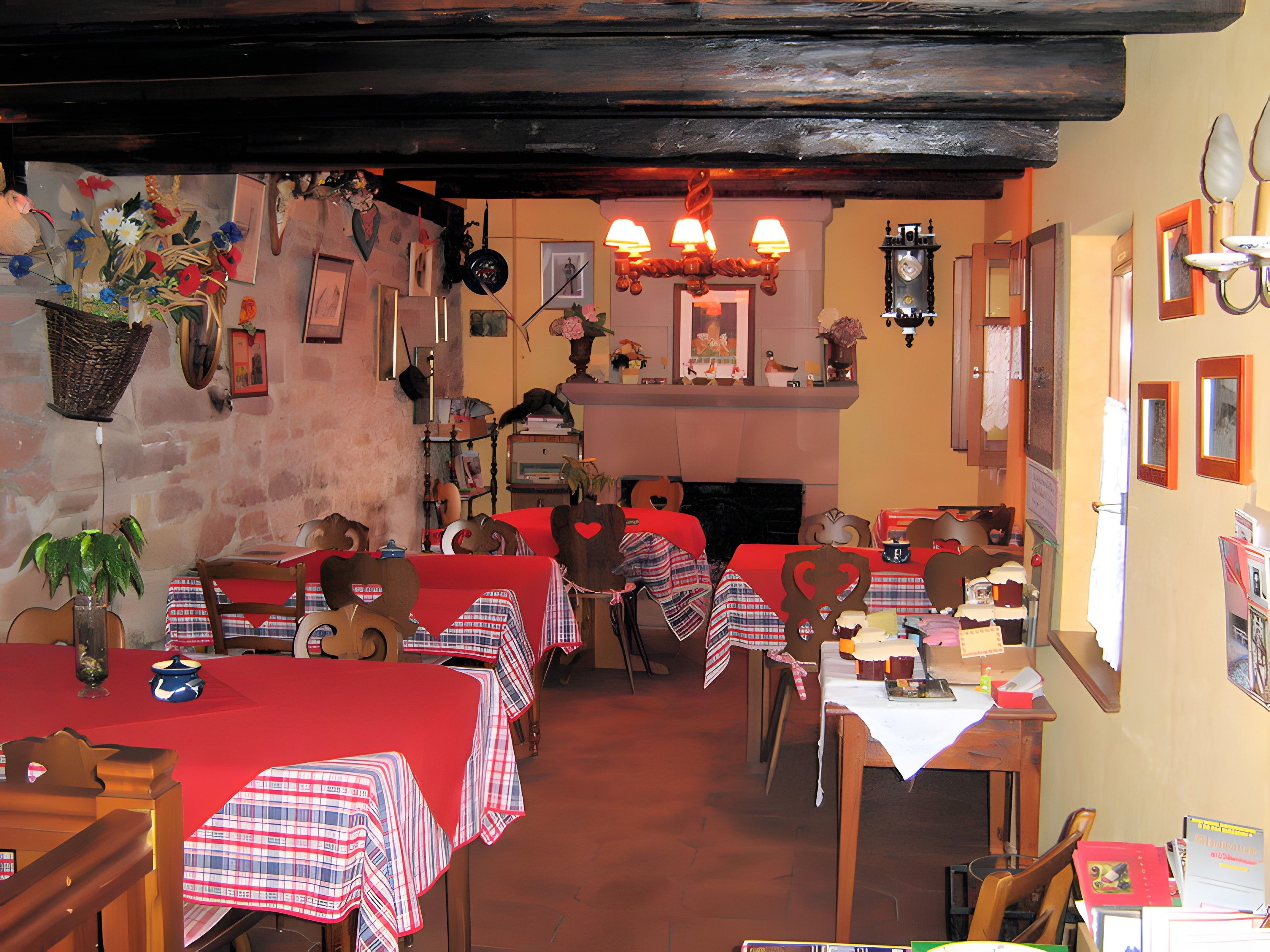 Un restaurant avec de nombreuses tables recouvertes de nappes à carreaux rouges et blancs, des chaises en bois et une variété de décorations murales, notamment des tableaux encadrés et une horloge.