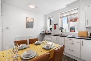 A modern kitchen with white cabinets, a dining table set for four, and a window with a view of the sky. - Hastings Vibe | By My Getaways (Hastings)