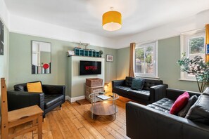 A living room with two black leather sofas, a wooden coffee table, a flat-screen TV mounted on the wall, and a yellow pendant light. - Hastings Vibe | By My Getaways (Hastings)
