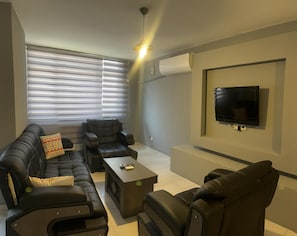 A modern living room with a sofa set, a coffee table, and a flat-screen TV mounted on the wall. - Masionette Home Village 4 (Bergheim)