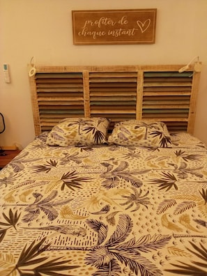 A bedroom with a wooden headboard, a bed with patterned bedding, and a wall-mounted sign with text.