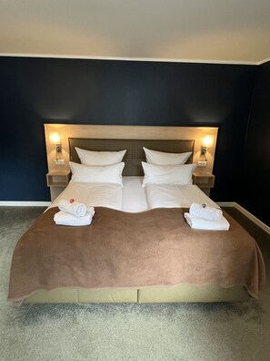 Ein Doppelbett mit brauner Bettdecke, zwei weiße Kissen und zwei Nachttischlampen.