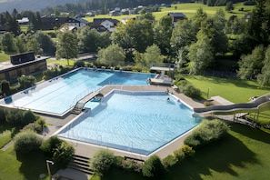 Un complex de piscines amb diverses piscines i un tobogan, envoltat de vegetació exuberant i edificis residencials.