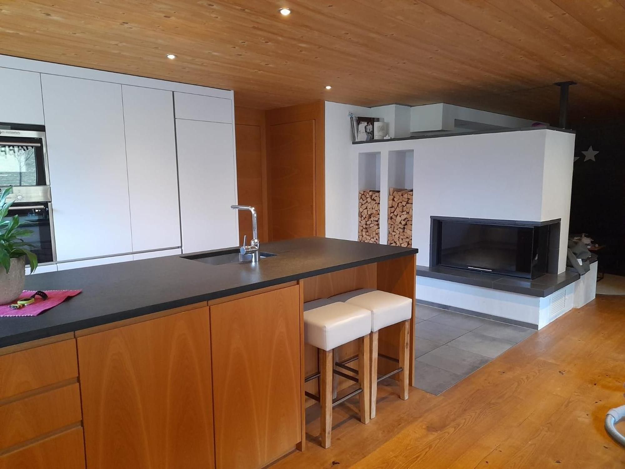 A modern kitchen with wooden cabinets, a black countertop, and a built-in fireplace.