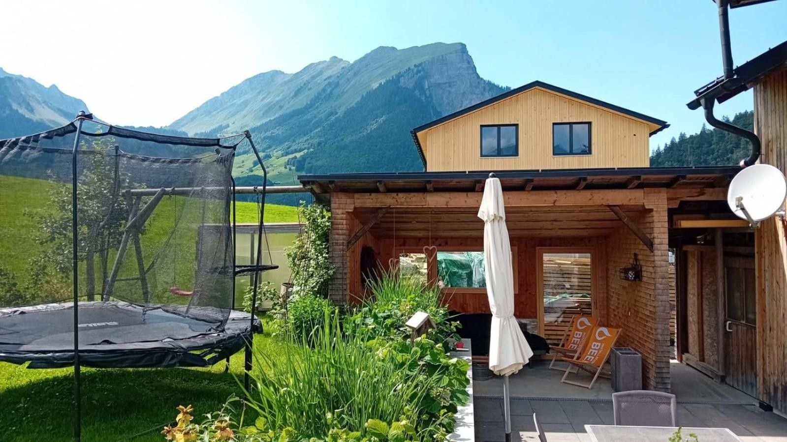 En træhytte med terrasse, trampolin og bjergudsigt.